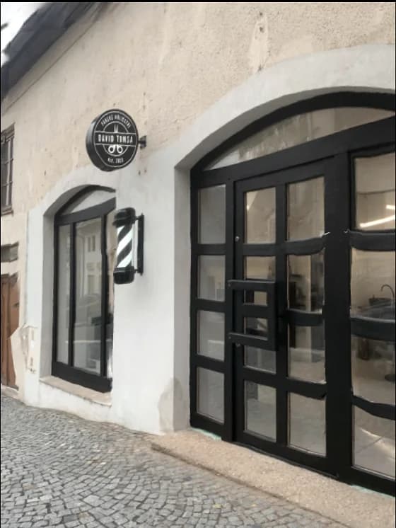 Klenutý vchod holičství s černými dveřmi a barber pole na bílé omítce